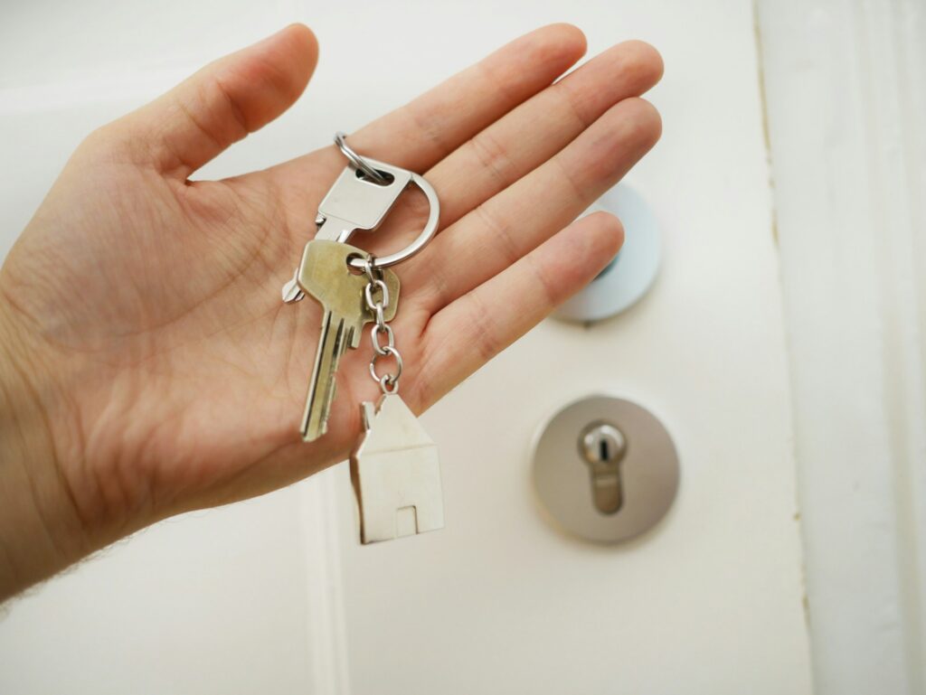 A hand holding a key ring with two keys and a little house keychain